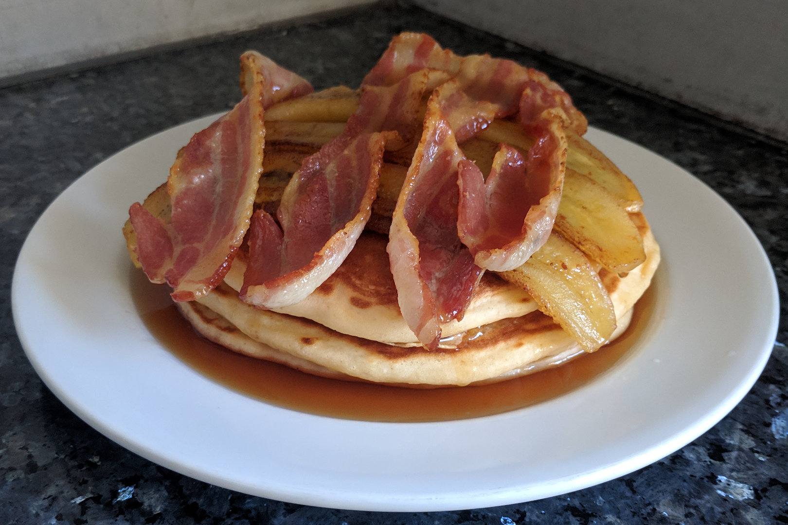 Image depicting three lusciously thick pancakes topped with bacon, banana and syrup